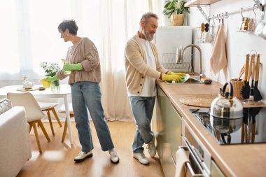 A mature couple shares joyful moments while washing dishes in their warm kitchen. clipart