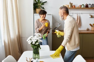 Olgun bir çift güneşli bir sabahta mutfağını temizlerken kahkahalarını paylaşıyor..