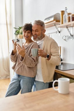 A couple enjoys a lighthearted moment together while holding drinks in their stylish kitchen. clipart