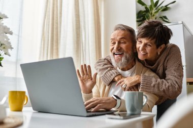 A mature couple shares laughter and warmth as they engage in an online conversation at home. clipart