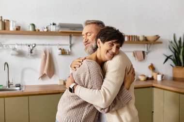 Two seniors express love and affection while hugging in a bright, inviting kitchen. clipart