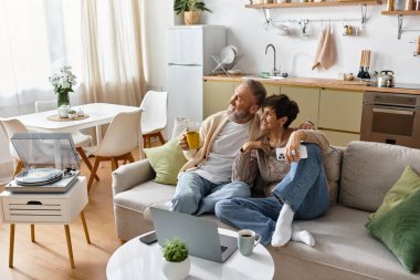 Couple relaxes on the couch, sharing warmth and laughter in their cozy living room. clipart