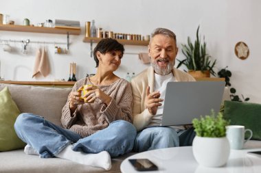 Olgun bir çift, dizüstü bilgisayarla uğraşırken koltuklarında oturup kahkahalarını paylaşıyor..