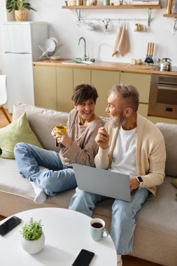 Oturma odasındaki dizüstü bilgisayarda çalışırken çiftler gülücüklerini ve içkilerini paylaşıyor..