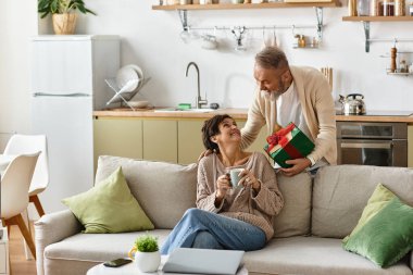 Olgun bir çift evde sıcak bir kutlamanın tadını çıkarır. Düşünceli bir hediye alışverişi ve gülümsemeyle..