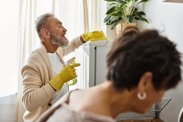 Mature couple shares joyful moments while cleaning and tending to their indoor plants.