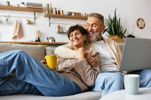 Зрелая пара делится теплым смехом и чаем в стильной гостиной, создавая радостные воспоминания.