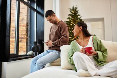 A beautiful couple relaxes in their decorated living room, sharing warmth and love during Christmas. clipart