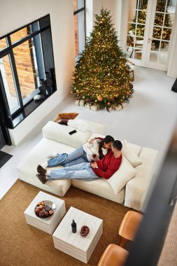 In a modern apartment, a couple enjoys a cozy moment together near a sparkling Christmas tree. clipart