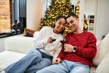 A couple enjoys warm drinks while surrounded by holiday decorations and a Christmas tree. clipart