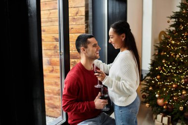 A couple joyfully enjoys each other's company while sipping wine in their decorated apartment. clipart