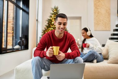 Bir çift Noel ağacının yanında rahatlar, sıcak içeceklerin ve arkadaşlığın tadını çıkarırlar..