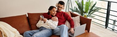 Couple enjoys quality time by a laptop while snuggled up on a cozy couch in winter, banner clipart