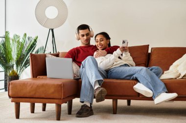 A couple relaxes together in stylish winter attire while sharing joyful moments on a couch. clipart