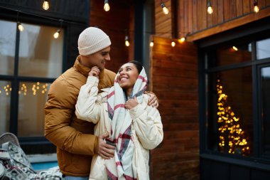 A couple enjoys a joyful winter moment together by twinkling Christmas lights and decorations. clipart