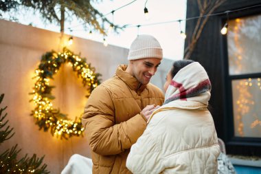 A beautiful couple shares a warm moment outdoors surrounded by Christmas decorations. clipart