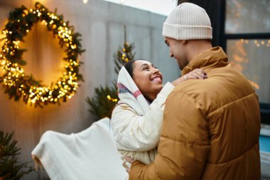 A couple in cozy winter clothes enjoys each other amid festive decorations. clipart