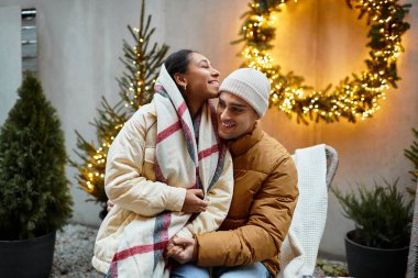 A couple enjoys each other's warmth while surrounded by twinkling holiday lights. clipart