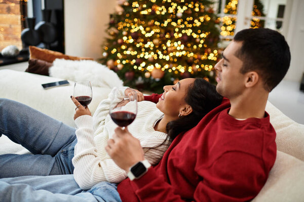 A couple enjoys quality time together, sipping wine in their holiday-decorated home.