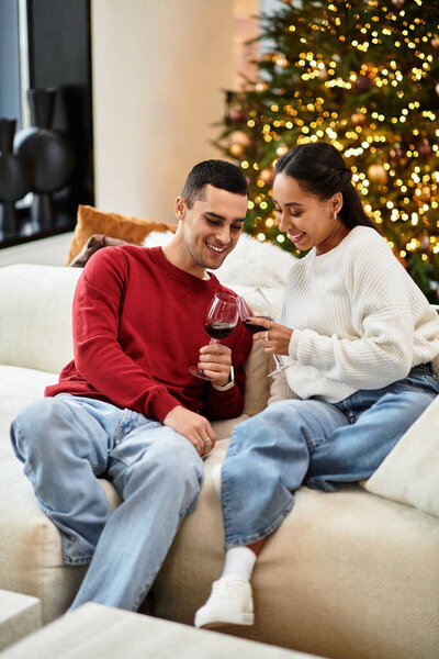 A loving couple shares laughter and joy by the Christmas tree in their stylish living room.