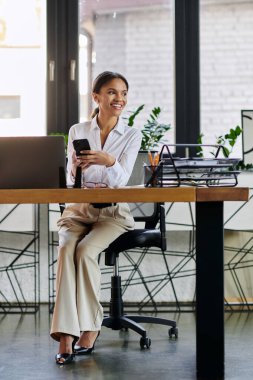 A young african american businesswoman engages with her phone in a bright modern workspace. clipart