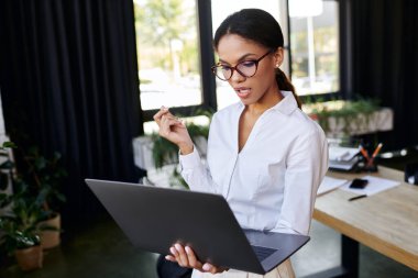 Beyaz gömlekli genç bir Afrikalı Amerikalı iş kadını laptopuyla meşgul, derin düşüncelere dalmış..