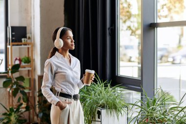 Beyaz gömlekli genç bir Afrikalı Amerikalı kadın ofiste kahve içerken yansıyor..
