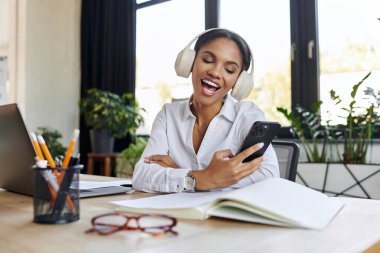 Genç bir Afrikalı Amerikalı iş kadını, parlak bir ofiste telefonunu kullanırken gülümsüyor..