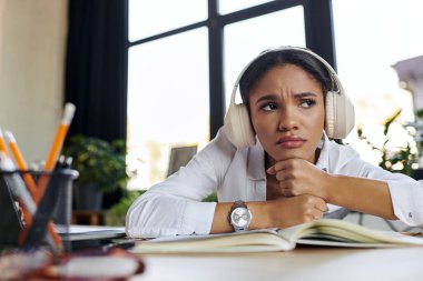 Beyaz gömlekli ve kulaklıklı genç profesyonel bir kadın ofiste üzgün hissediyor.