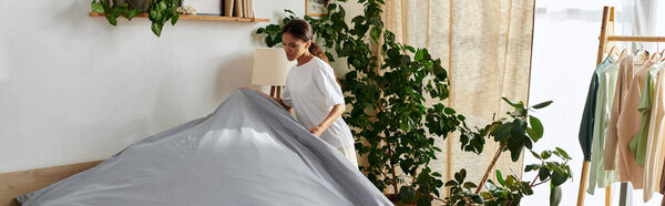 Молодая афроамериканка аккуратно расставляет постель в шикарной квартире, заполненной растениями, плакатами