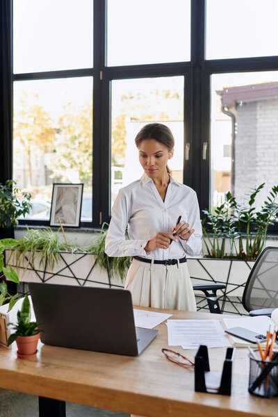 Молодая африканская американская бизнесвумен задумчиво стоит за своим столом в современном офисе.