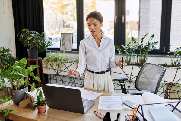 Молодая афроамериканская деловая женщина в белой рубашке фокусируется на своих задачах, стоя.