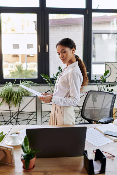 Молодая афроамериканка в белой рубашке просматривает документы за своим столом.