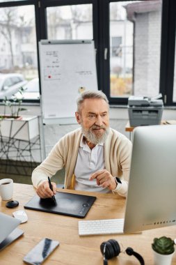 A mature man focuses on digital art in his office, surrounded by plants and a graphics tablet.