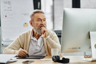 Kıdemli adam yaratıcı bir işle meşgul, derin düşüncelere dalmış, ofis aletleri ve teknolojiyle çevrili..