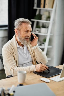 Yakışıklı, yaşlı bir adam şık masasında otururken gülümsüyor.