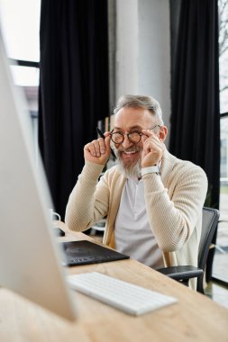 Yakışıklı son sınıf öğrencisi gülümsüyor ve bilgisayarına odaklanırken gözlüklerini ayarlıyor..