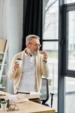Yakışıklı, olgun bir adam masasında kahvesini yudumlarken mola verir.
