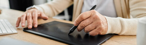 Handsome senior man draws on a tablet while seated at a stylish wooden desk.