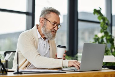 Son sınıf öğrencisi laptopuna odaklanmış, ofiste verimli bir seans sırasında kahvesini yudumluyor..