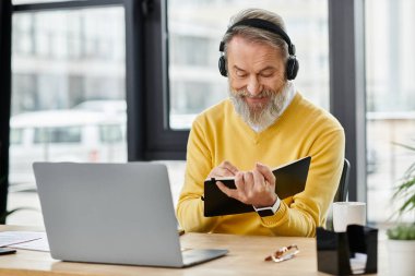 Kulaklıklı yakışıklı, olgun bir adam modern bir kafede masa başında otururken notlar yazıyor..