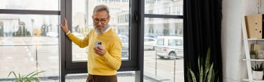 Sarı kazaklı beyefendi şehir manzarasına bakarken telefonunu kontrol ediyor..