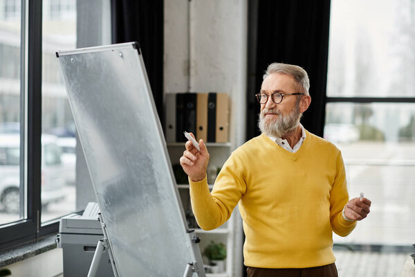 Handsome senior man engages an audience while pointing at a whiteboard in an office.