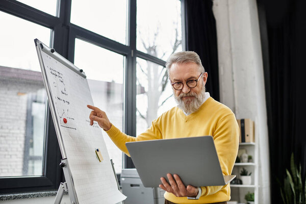 Handsome senior man shares insights while using a laptop in a well lit office setting.