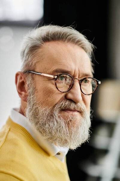 Mature man wearing glasses and a yellow sweater gazes thoughtfully in a warm space