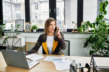 Çekici genç kadın, moda bir ofis ortamında raporları incelerken telefonda konuşuyor..