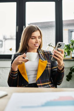 Parlak çalışma alanı, genç profesyonelin kahvesini yudumlaması ve akıllı telefonunu kontrol etmesi içeriyor..