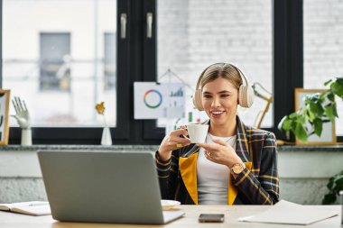 Kareli ceketli çekici bir kadın kahvesini yudumlarken gülümsüyor ve laptopuna odaklanıyor..