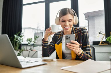 Şık bir profesyonel telefonuyla ilgileniyor ve mesai saatlerinde kahvenin tadını çıkarıyor..