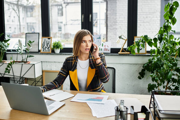 Привлекательная молодая женщина говорит по телефону, анализируя отчеты в модном офисе.